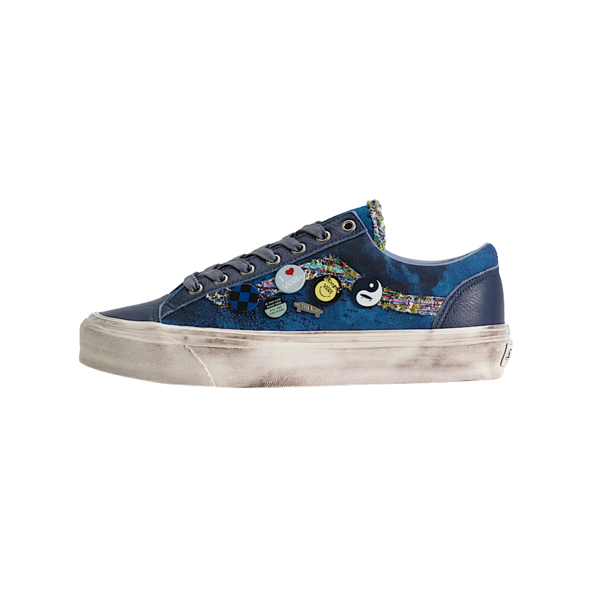 A low-top sneaker in navy blue canvas with a colorful abstract pattern on the side, decorated with several small circular pins, featuring a distressed off-white sole.