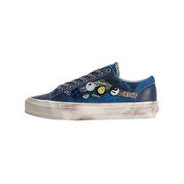 A low-top sneaker in navy blue canvas with a colorful abstract pattern on the side, decorated with several small circular pins, featuring a distressed off-white sole.
