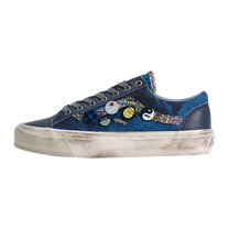 A low-top sneaker in navy blue canvas with a colorful abstract pattern on the side, decorated with several small circular pins, featuring a distressed off-white sole.